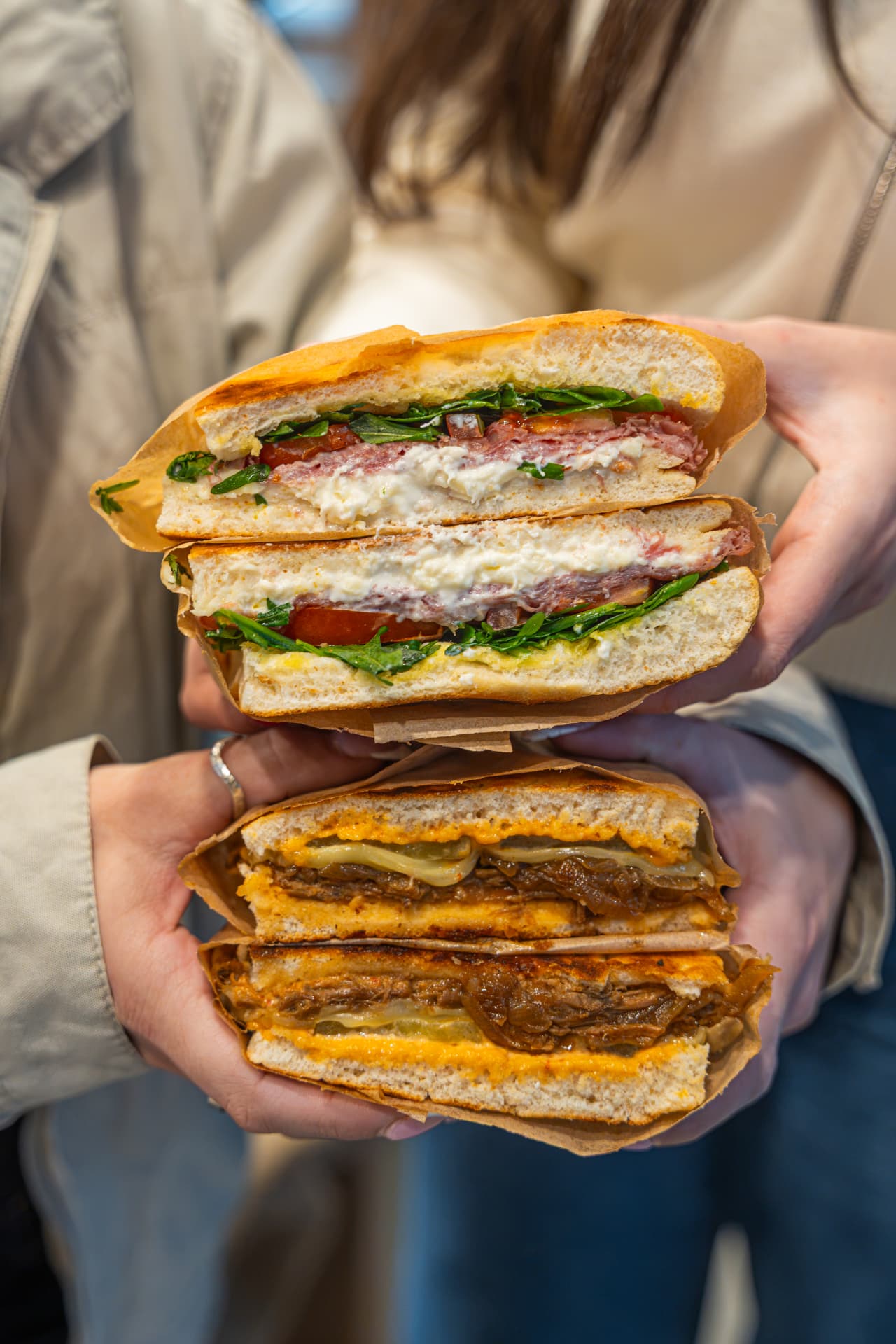 Two hands holding freshly pressed focaccia sandwiches at Miro's Deli.